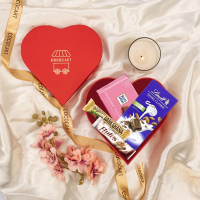 Heart-throb Hamper of Lindt Swiss Classic chocolates with a candle and flowers on silk fabric, viewed from above.