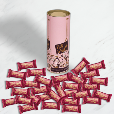 A large canister of Whittakers Loose Cranberry & Almond Mini Slab 100/200gm surrounded by numerous small, individually wrapped chocolates with dark bittersweet chocolate and Californian almonds on a marble surface.