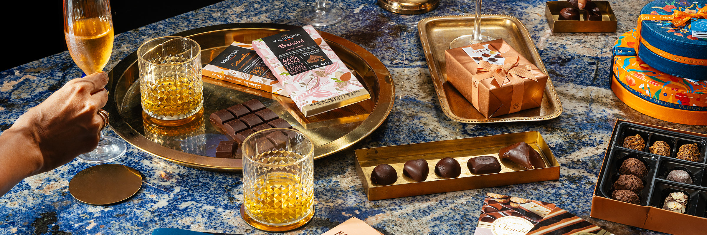 A person is holding a glass of champagne and chocolates on a table.