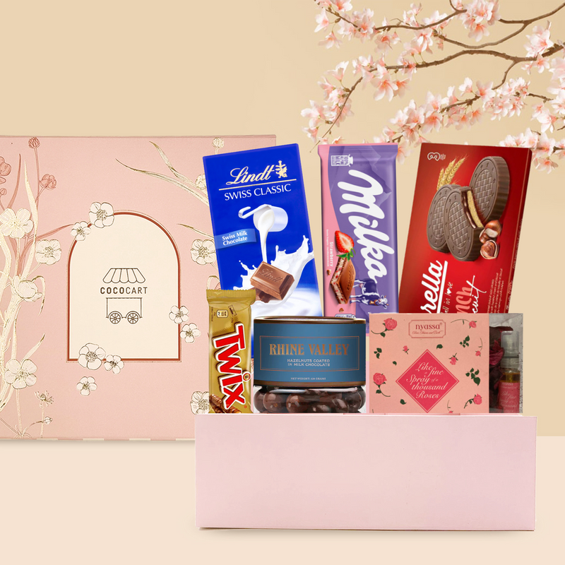 An assortment of international chocolates including milk chocolate, displayed beside a pink gift box with a cherry blossom background. Brands visible include Lindt, Milka, and Twix. - The Sakura Hamper by Gift Hampers.