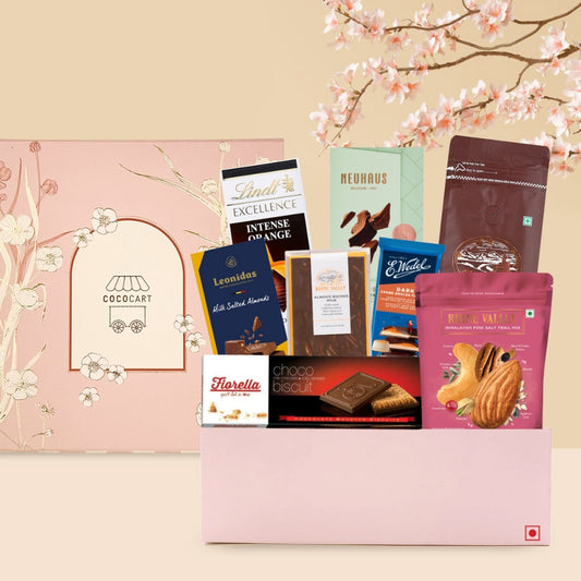 Presenting The Sakura Premium Hamper by Gift Hampers, featuring a delightful assortment of Lindt Excellence Orange Intense, Neuhaus Milk 35% Cocoa, and Leonidas Milk Almonds & Sea Salt, beautifully set against a charming floral backdrop.