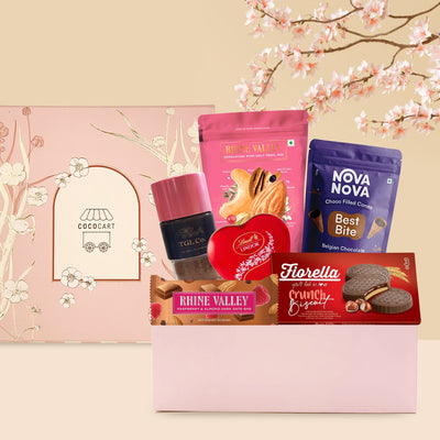 Assorted gourmet Unconditional Love - Mother's Day Collection chocolates and cookies displayed with a pink gift box, set against a soft peach background with cherry blossoms.