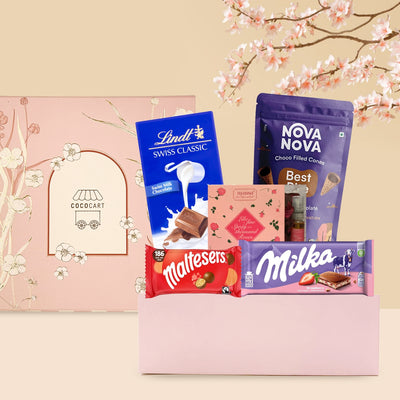 A gift box with assorted chocolates including Lindt Swiss Classic, maltesers, and Milka Strawberry Milk Chocolate from the Sweet Treat - Mother's Day Collection, displayed against a pastel background with cherry blossoms. Brand Name: Gift Hampers