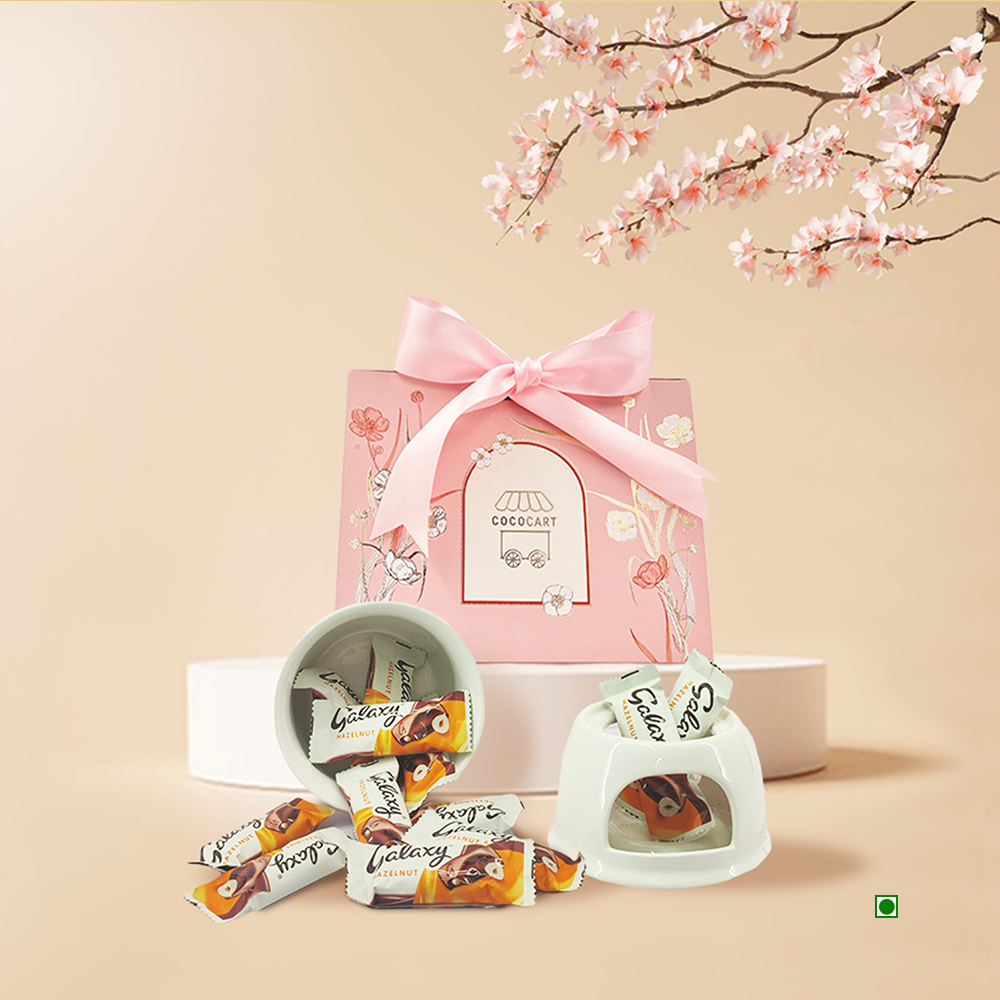 The Mini Galaxy Sakura Hamper by Gift Hampers, presented in a pink gift box adorned with a ribbon and cherry blossoms, features an elegant assortment of chocolates including Galaxy Minis, artfully arranged in white bowls.