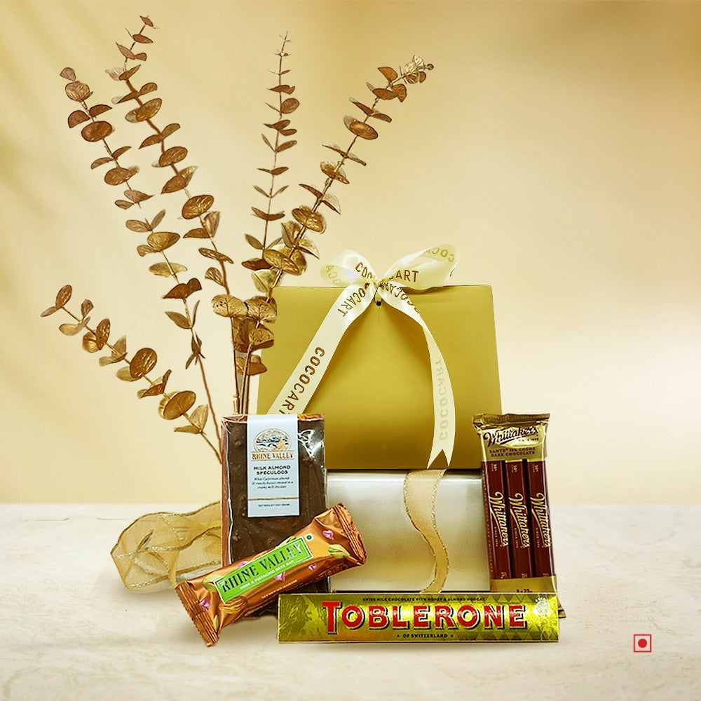 Experience the **Happiness & Celebration hamper** by **Gift Hampers**, featuring two gold-wrapped boxes with ribbon, containing Toblerone, a Nature Valley granola bar, a Rose & Pistachio Date Bar, a coffee pack, chocolate sticks, and adorned with decorative dry foliage on a beige background.