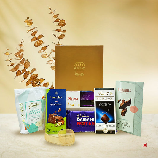 The Premium Festive Opulence Hamper by Gift Hampers is a luxurious collection of international chocolates and snacks, elegantly displayed in front of a shimmering gold gift box, featuring an exquisite array of various brands and flavors.