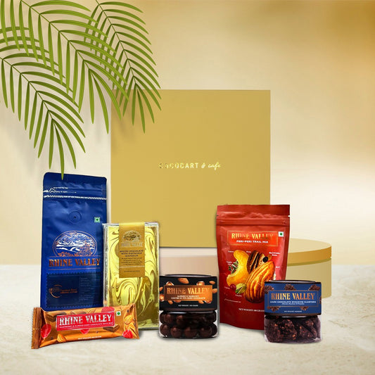 Gift Hampers' Rhine Valley Christmas Magic features delectable chocolates and flavorful pasta elegantly displayed before a yellow gift box with a decorative palm leaf, perfect for those who love international flavors with an Indian twist.