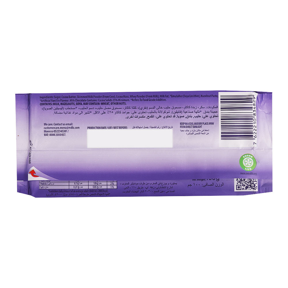Back view of a Milka Alpine Milk Bar 100g wrapper displaying the ingredients, nutritional information, and barcode. The wrapper is mainly purple with white and multilingual text, highlighting its Alpine milk chocolate heritage from Germany.