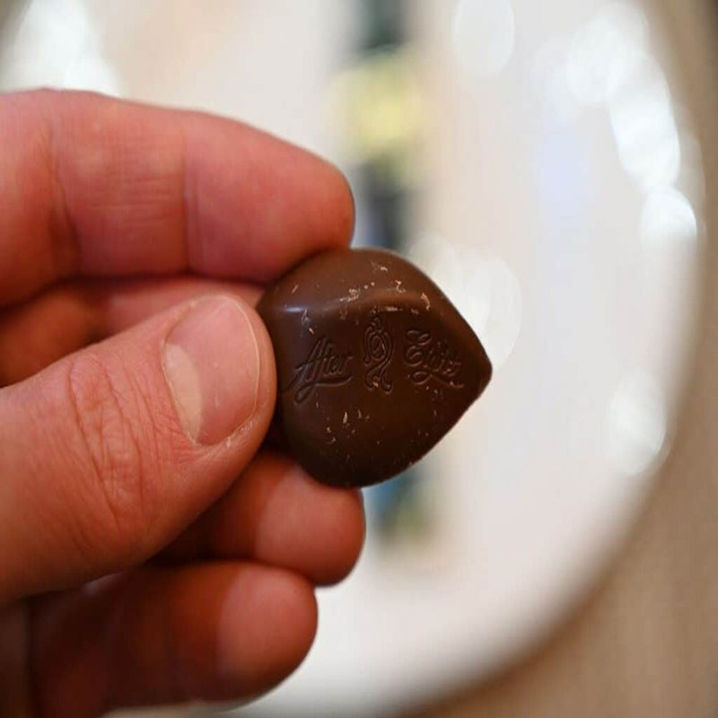 A person holding a piece of After Eight Mini Snack Bag 150g chocolate on top of a plate.