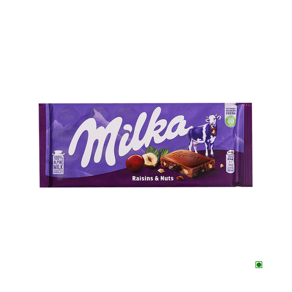 A Milka Raisin and Nut Bar 100g wrapper featuring the "Raisins & Nuts" flavor, with a purple background and an image of a cow, showcasing smooth milk chocolate filled with hazelnut pieces.