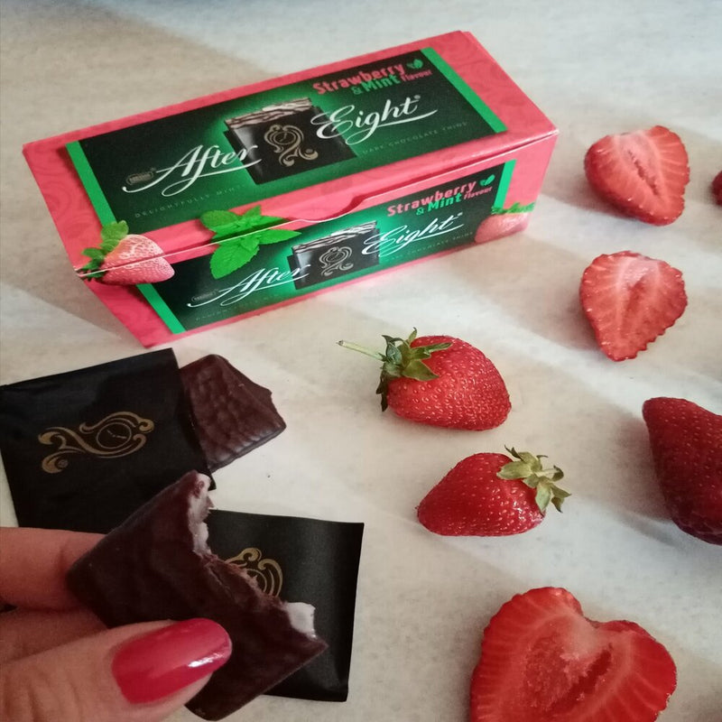 A person is holding a box of After Eight Strawberry Mint Chocolate Thins Box 200g with strawberries on it.