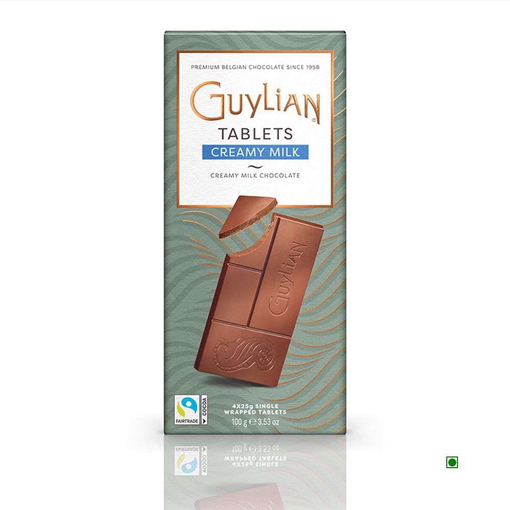 The packaging of the Guylian Creamy Milk Chocolate Tablet 100g, made in Belgium, features a partially unwrapped section showcasing the smooth chocolate within, along with prominent Fairtrade and vegetarian labels.