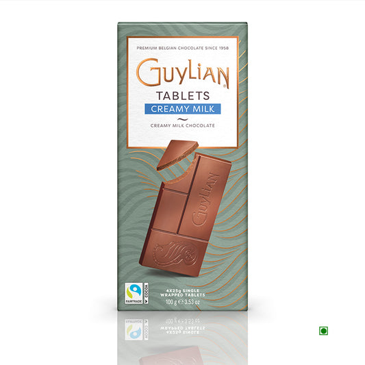 The packaging of the Guylian Creamy Milk Chocolate Tablet 100g, made in Belgium, features a partially unwrapped section showcasing the smooth chocolate within, along with prominent Fairtrade and vegetarian labels.