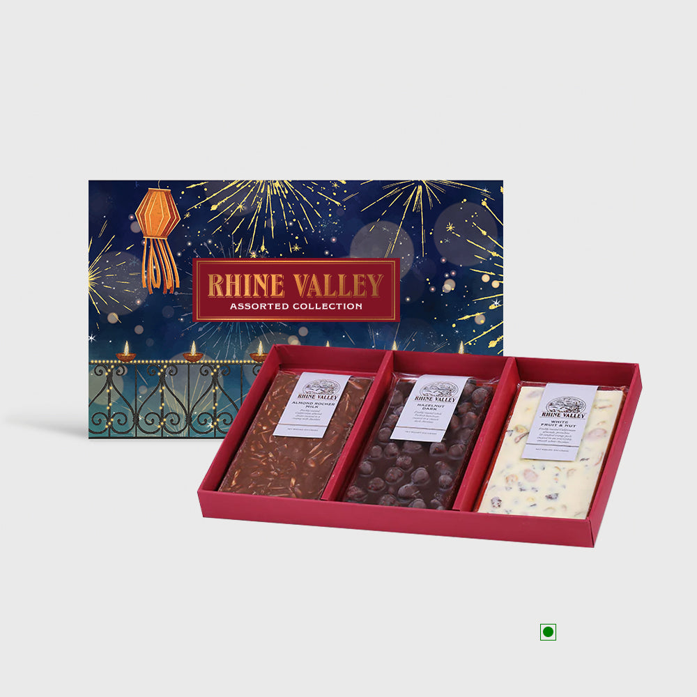 The Rhine Valley Milk, Dark & White Assorted Collection 300g features three gourmet chocolate bars, including the exquisite almond rocher milk variety, elegantly arranged in a red tray with a decorative fireworks backdrop.