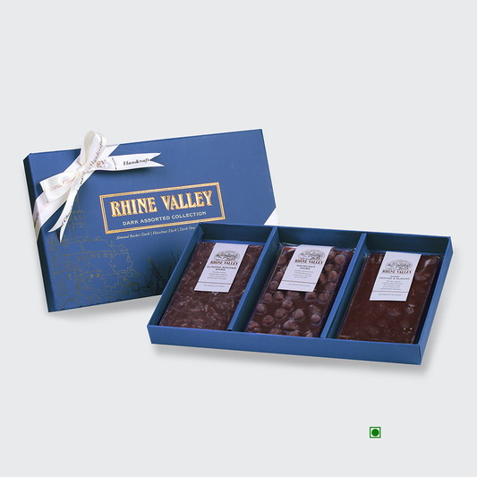 A blue box of Rhine Valley Dark Assorted Collection 300g, featuring three assorted chocolate bars, is elegantly open and tied with a white ribbon.