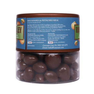 A clear container of Rhine Valley Macadamia & Pistachio Milk Dragees 100g chocolates, with product and nutritional information labels visible.