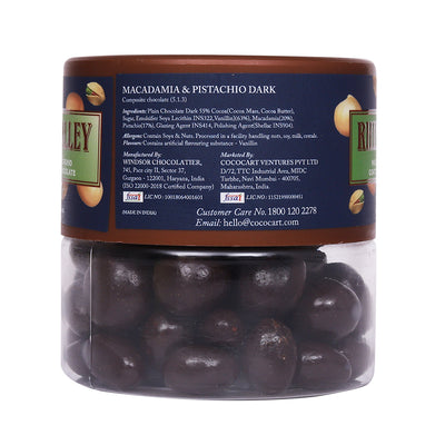 A jar of Rhine Valley Rhine Valley Macadamia & Pistachio Dark Dragees 100g containing chocolate-covered nuts, with ingredient list and company contact info on the label.