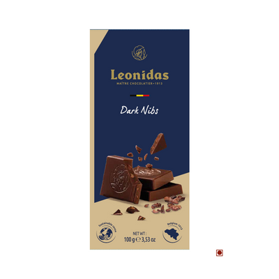 A Leonidas Dark 54% Nibs Roasted Cocoa Beans Bar package labeled "dark nibs" with pieces of Belgian chocolate and cacao nibs scattered around, against a navy and beige background.