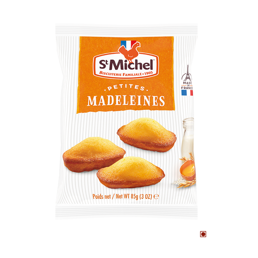 A package of St Michel Mini Madeleines Sponge Cake Bag 85g is shown. The 85-gram (3-ounce) bag contains the French baked goods, featuring an image of three golden-brown madeleines, a bottle of milk, and vanilla. These delicious treats are made in France with cage-free eggs.