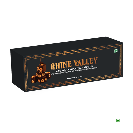 A black box labeled "Rhine Valley" contains Gianduja chocolate cubes with 70% dark chocolate, made from cocoa sourced from India. The packaging showcases a gold and brown design enhanced with images of mouth-watering chocolate pieces.