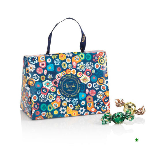 The Venchi Murrine Gift Bag 150g features a vibrant floral design inspired by Venetian artisans, adorned with the Venchi logo, and includes two assorted wrapped candies in front.