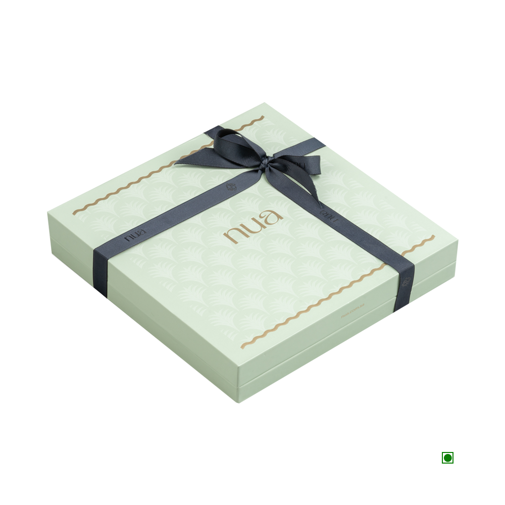 A light green square gift box adorned with a black ribbon, featuring the word "Nua" on the lid. This luxurious mint gift originates from Saudi Arabia and is known as the Nua Luxury Nakheel Mint Gift Box 500g by Nua.