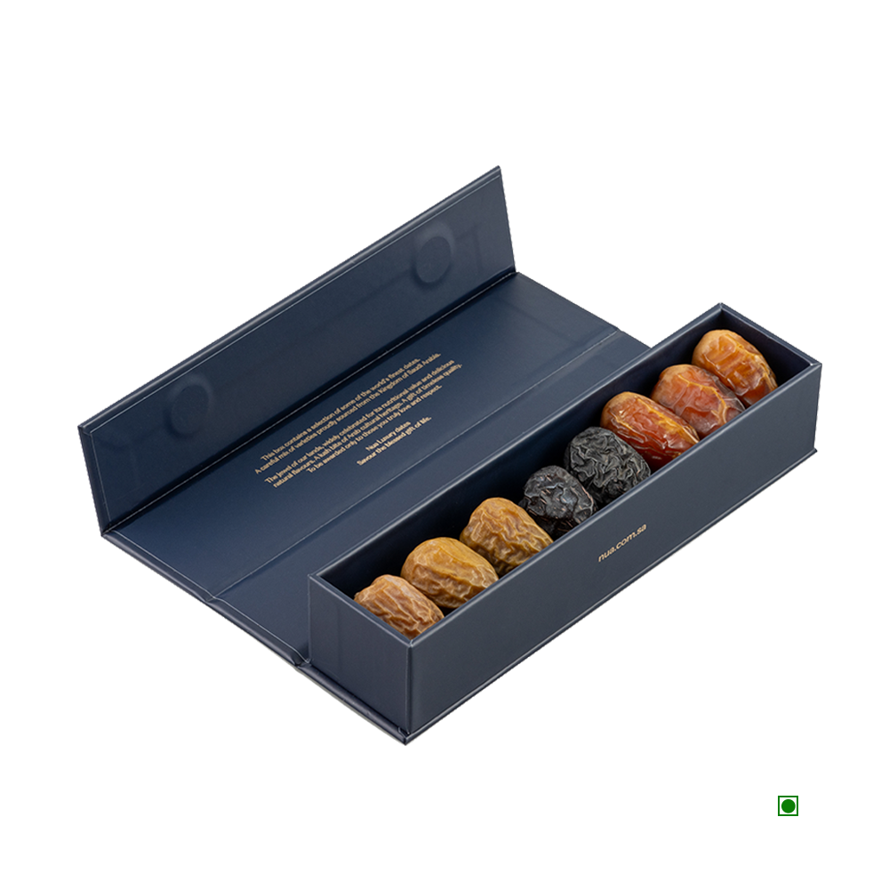 A Nua Small Gift Box Navy Fronds 100g, featuring nine assorted dates neatly arranged in a single row with the lid open to display text inside. These exquisite dates, proudly originating from Saudi Arabia, come in a stylish blue box.