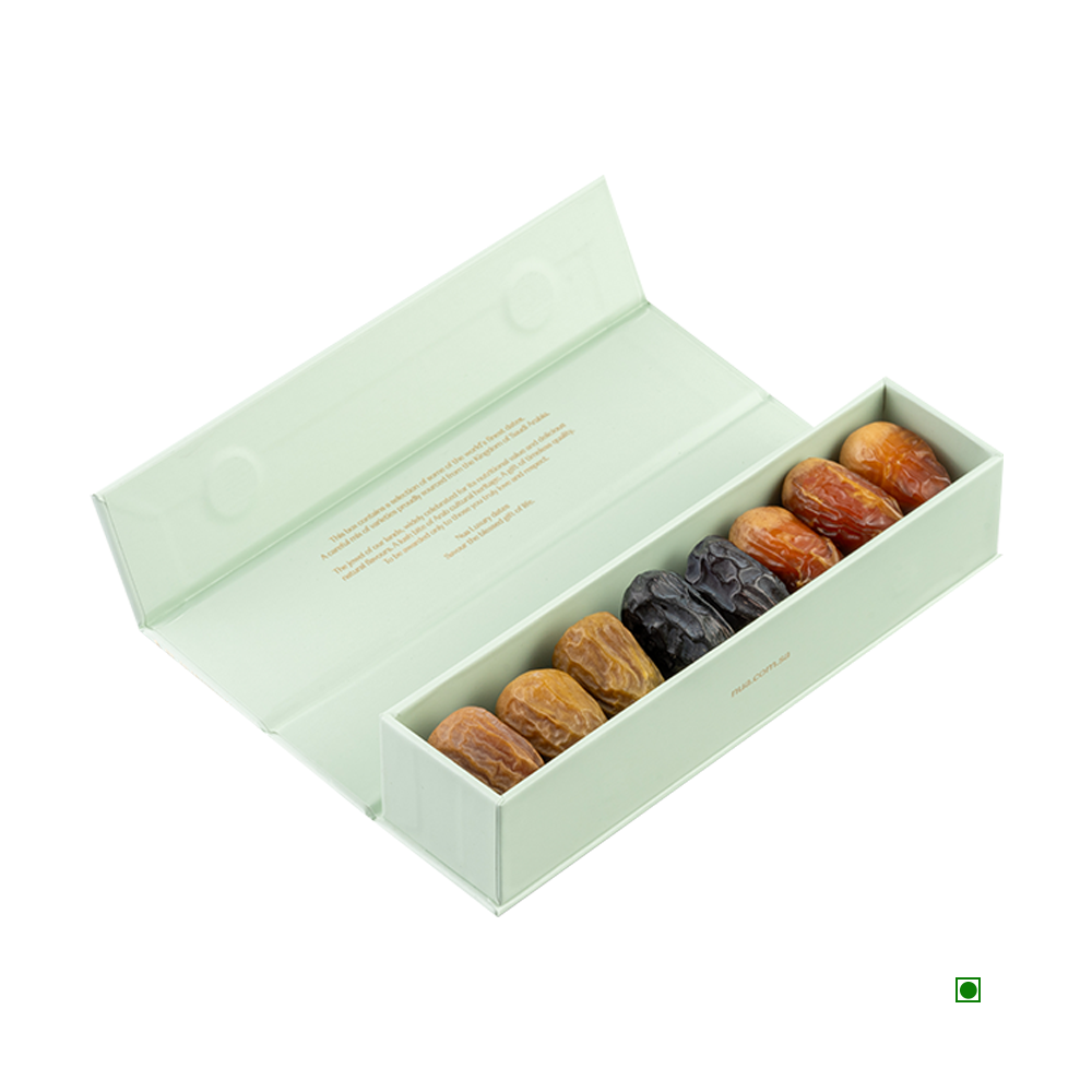 A Nua Small Gift Box Green Fronds 100g, featuring a rectangular design with an open lid, displays a row of various types of dates in assorted colors and textures, proudly showcasing their Country of Origin: Saudi Arabia.