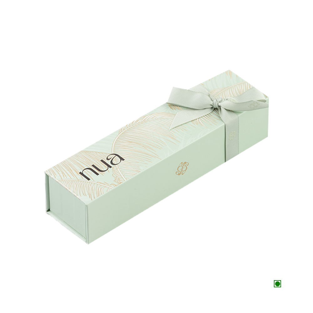 A rectangular pastel green box with a light palm leaf design, featuring the word "Nua" on the top, tied with a matching ribbon, and proudly showcasing its Country of Origin: Saudi Arabia. The product is known as the Nua Small Gift Box Green Fronds 100g.