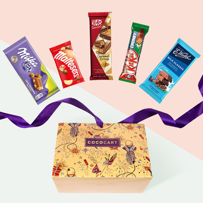 A box filled with The Sunshine Gold : Pyramid chocolate bars and a purple ribbon from Gift Hampers.