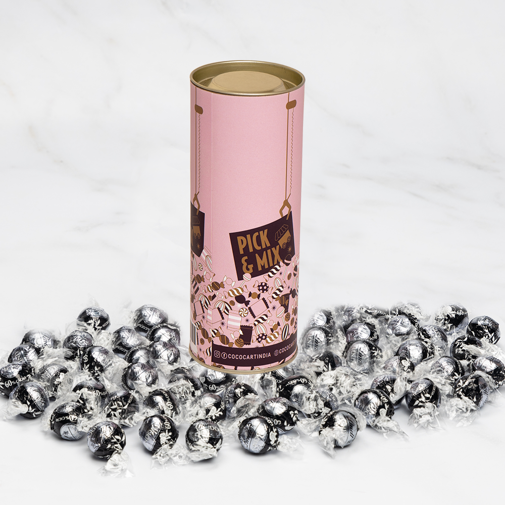 A cylindrical container labeled "Pick & Mix : Lindor Extra Dark 250/500g" stands upright, surrounded by numerous individually wrapped Lindt truffles on a white marble surface.