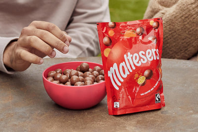 A person is holding a Malteser Milk Pouch 175g next to a bowl.