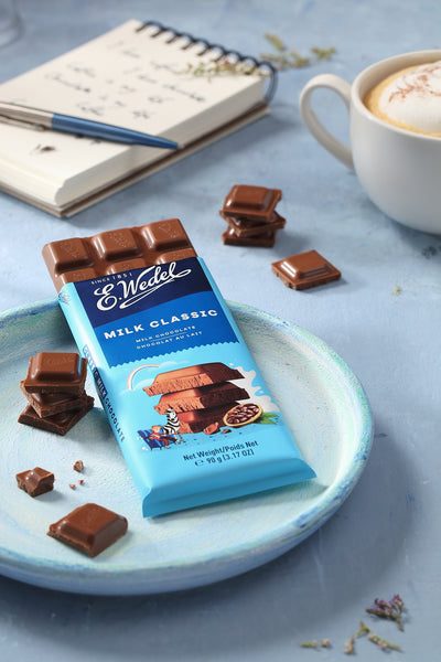 A Wedel Milk Chocolate Bar 90g sits on a plate next to a cup of coffee.