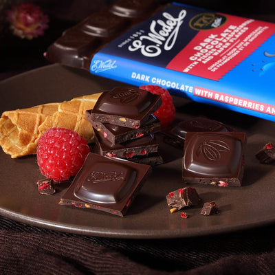 A plate with Wedel Dark Choc With Raspberry & Wafers Bar 80G and raspberries on it.
