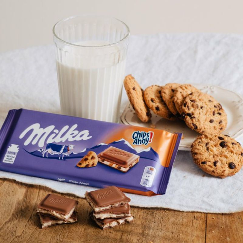A Milka Chips Ahoy Bar 100g, cookies and a glass of milk on a table.