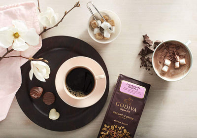 A cup of Godiva Chocolate Truffle Coffee 284g with marshmallows and flowers on a table.