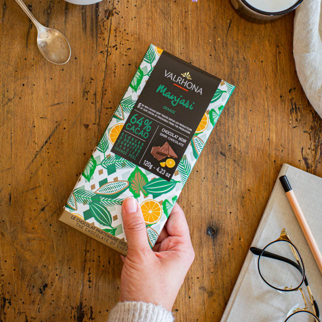 A person holding a Valrhona Manjari Orange Peel 64% Bar 120g on a table.