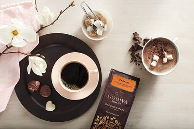 A cup of Godiva Caramel Coffee 284g and a chocolate bar on a table.