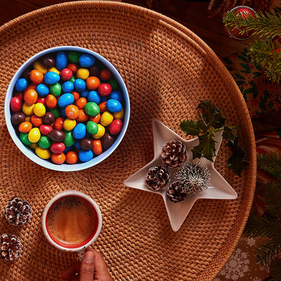 A person is holding a cup of coffee and a bowl of M&M's Peanut Pouch 250g.
