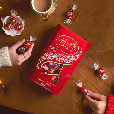 A woman in Switzerland is holding a box of Lindt Lindor Milk Cornet 200g chocolates, creating an irresistibly smooth moment.