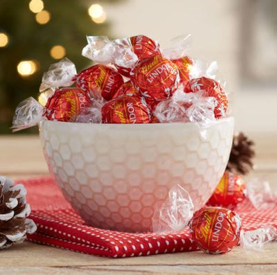 A bowl of Lindt Lindor Milk 100/250/500g candy canes sitting on top of a Christmas tree.