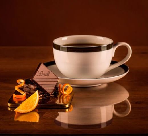 A cup of coffee and Lindt Excellence Orange Intense Bar 100g on a table.