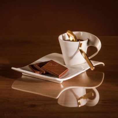 A cup of coffee with a spoon and Lindt Excellence Extra Creamy Bar 100g.
