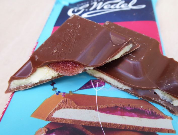 A Wedel Milk Chocolate With Blueberry & Wild Strawberry Filling Bar 100g with a piece cut out of it.