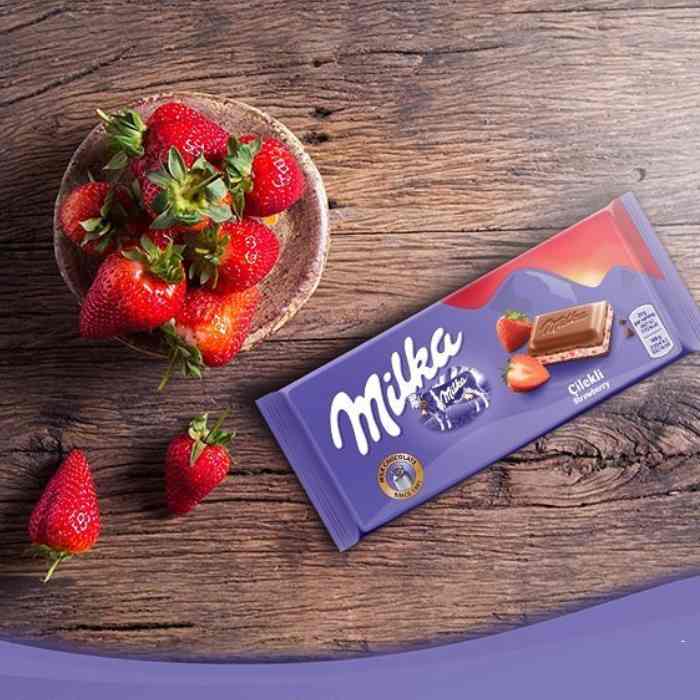 A Milka Strawberry Milk Chocolate Bar 100g with strawberries on a wooden table.