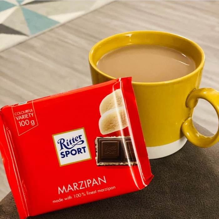 A cup of coffee next to a box of Ritter Sport Marzipan Bar 100g.