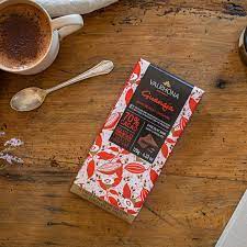 A Valrhona Guanaja Cocoa Nibs 70% Bar 120g sitting on a table next to a cup of coffee.