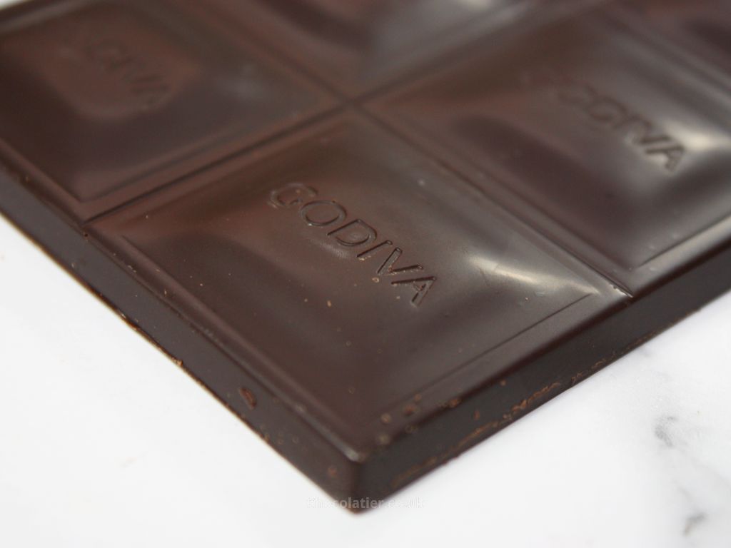 A close-up of the Godiva Dark 90% Bar 90g, with "Godiva" embossed on each square, lies elegantly on a light surface, showcasing its rich Belgian heritage.